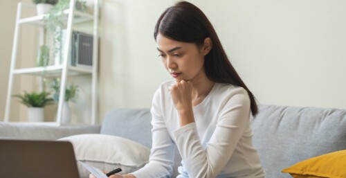 Person Reviewing Paperwork on Couch with Laptop